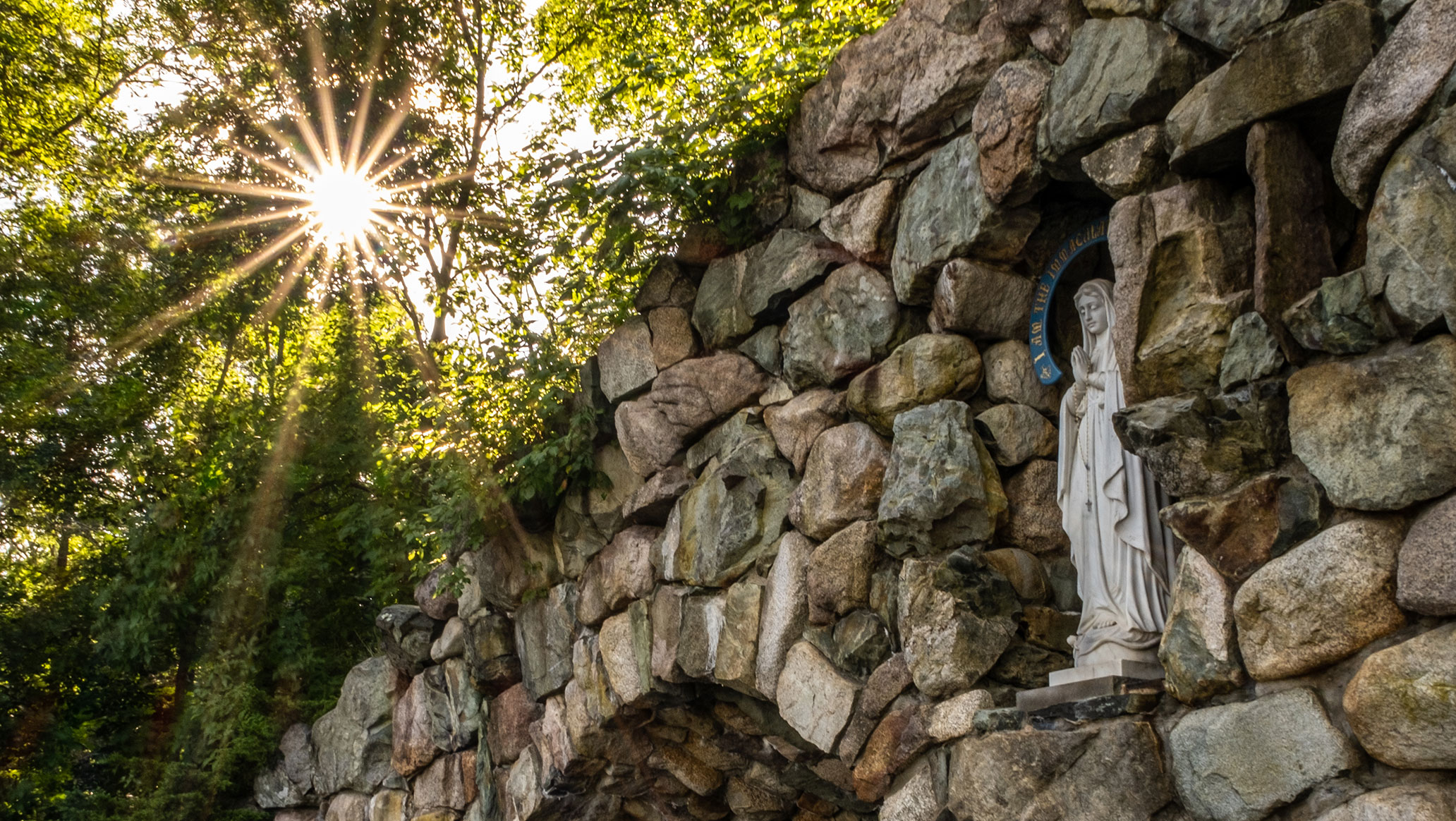 Photo of a statue at Stonehill College with light shining through the trees